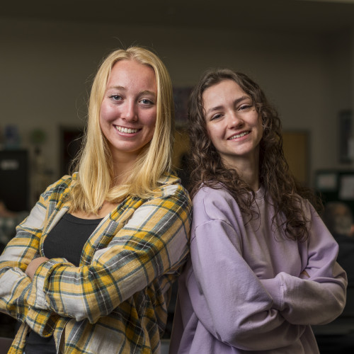 Two students smiling with arms crossed, standing back-to-back